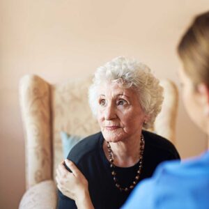 Older adults perform seated and standing exercises with light weights in a bright communal room.